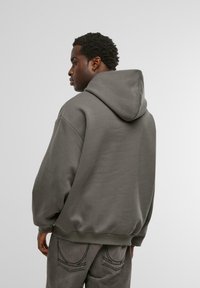 Šedá mikina s kapucňou, uvoľnený strih, mäkká štruktúra a ozdobné manžety. V kombinácii s nohavicami v rovnakom štýle s kontrastnými švami.