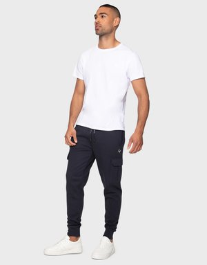 Camiseta blanca de cuello redondo, joggers de carga navy con bolsillos laterales, puños elásticos y zapatillas blancas. Diseño simple y ajustado.