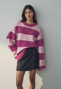 Übergroßer pullover mit pink und weißen Streifen aus strukturiertem Stoff, kombiniert mit einem schwarzen, faux Leder Wickelrock, der sichtbare Nähdetails aufweist.