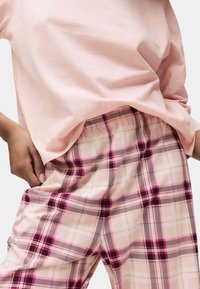 Helles rosa Baumwoll-T-Shirt kombiniert mit karierten Schlafanzughosen in Pink, Schwarz und Weiß, mit einem elastischen Bund und einem lockeren Schnitt.