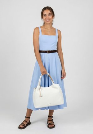 Woman wearing a light blue sleeveless dress with a brown belt, black sandals, and holding a large white handbag with rope handles.