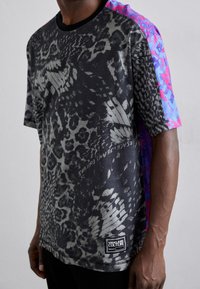 Kortärmad skjorta med en mörk, strukturerad djurtryck och ljusrosa och blå accenter på axlarna. Etikett längst ner till vänster.