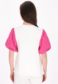 Tričko s krátkým rukávem, které má bílou barvu a růžové, texturované rukávy s houndstooth vzorem. Kulatý výstřih a volnější střih.