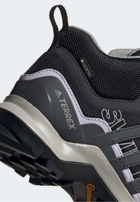 Gros plan sur une chaussure de randonnée Adidas Terrex noire et grise avec une étiquette Gore-Tex et une semelle en caoutchouc Continental robuste.