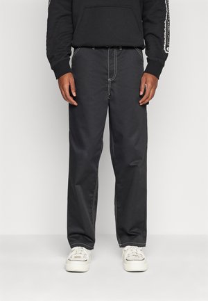 Black loose-fitting pants made of durable fabric with contrasting white stitching. Features side pockets and an elastic waistband.