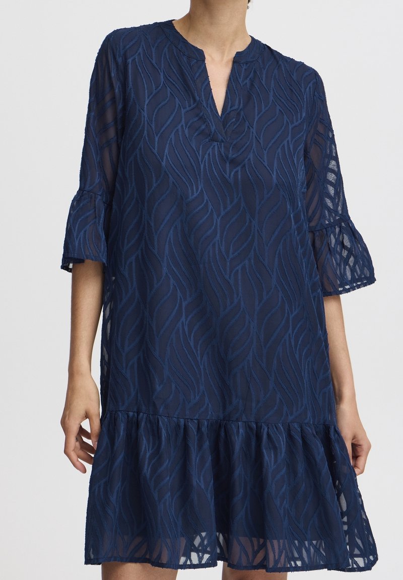 Laivansiniset kerrokselliset mekko, jossa on tekstuurinen lehden kuvio, V-mallinen kaula-aukko ja leveät 3/4-hihat, valmistettu kevyestä, läpikuultavasta kankaasta.