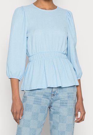 Lichtblauwe, gestructureerde blouse met lange mouwen, elastische taille en opgeblazen mouwen, gecombineerd met lichtblauwe geruite spijkerbroek.