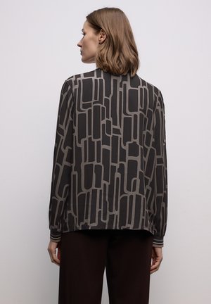 Bluzka z długim rękawem wykonana z lekkiego materiału w ciemnym brązie z geometrycznym wzorem w jasnoszarym kolorze. Posiada prosty kołnierzyk i detale mankietów.