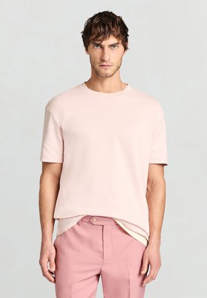 T-shirt rosa chiaro a maniche corte in tessuto morbido, scollo tondo, vestibilità rilassata, indossata con pantaloni rosa chiaro, design minimalista e senza motivi visibili.
