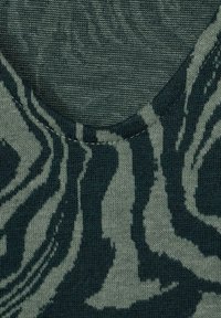 Close-up of textured fabric with a green and dark teal abstract zebra stripe pattern and a round neckline seam.
