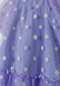 Robe en tulle violet avec des marguerites blanches brodées et des centres jaunes. Présente des volants superposés au niveau de l'ourlet. Texture douce et légère.
