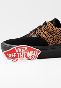 Černé semišové tenisky s hnědým vzorovaným svrškem, vybavené černými tkaničkami a plochou černou podrážkou. Obsahuje červenou a bílou cedulku "Vans Off The Wall".
