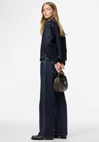 Jeans obleka v temnem odtenku, okrašena z metalnimi zakovami ob šivih. Kombinirana z majhno rjavo ročno torbico in črnimi škornji.