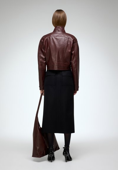 Cropped burgundy leather jacket over a long black skirt, held with a brown leather bag, paired with black ankle boots and tights.
