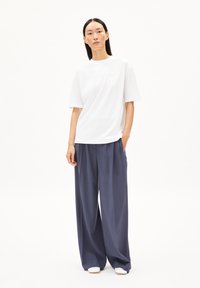 Vit t-shirt med kort ärm och rund hals, kombinerad med löst sittande marinblå byxor. Outfitten har en minimalitsk design och avslappnad passform.