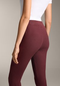 Leggings a coste bordeaux con vita alta, caratterizzati da una superficie testurizzata e un design aderente, mostrati da dietro su uno sfondo neutro.