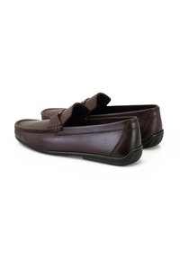 Bruine leren loafers met een gladde textuur, voorzien van een voorband en kleine ronde hardwareaccenten. Zwarte rubberen zool voor grip.