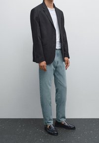 Black linen blazer over a white shirt, paired with light blue jeans and black loafers. Smooth texture and tailored fit throughout.