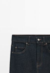 Dark blue denim jeans waist with visible button, belt loops, front pockets, and contrast orange stitching on a white background.