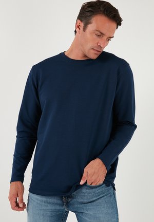 Marineblaues langärmeliges T-Shirt aus glattem Material, mit Rundhalsausschnitt und geradem Saum, kombiniert mit hellblauen Jeans.