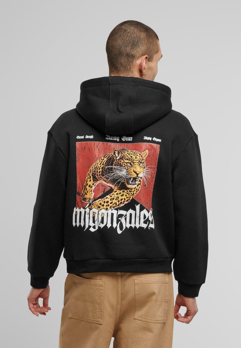 Schwarzer Kapuzenpullover aus weichem Stoff mit einem großen, bunten Leopardenmotiv auf dem Rücken und dem Text "migonza1es" in fetten weißen Buchstaben.