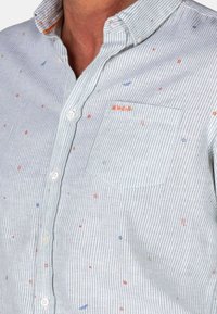 Gestreepte button-up blouse in lichtgrijs en wit, met kleurrijke bloem- en bladvormen, een borstzak en contrasterende kraagdetails.