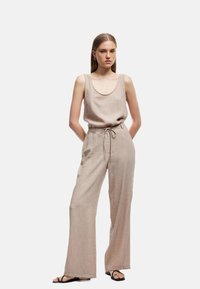 Top de lino beige sin mangas con un escote amplio, combinado con pantalones de pierna ancha de tiro alto a juego. El conjunto cuenta con una cintura con cordón.