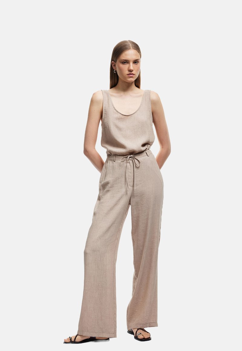 Top de lino beige sin mangas con un escote amplio, combinado con pantalones de pierna ancha de tiro alto a juego. El conjunto cuenta con una cintura con cordón.