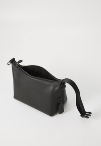 Svart lærveske med en teksturert overflate, glidelås lukking, justerbar stropp og en liten metalltag. Kompakt og vinkelrett design.