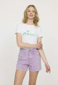 T-shirt blanc avec un graphique coloré de palmier, associé à un short en denim violet clair. Le short a une taille haute et des poches avant.
