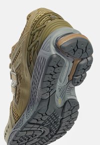 Baskets avec une tige verte et beige présentant un design en maille, un bout renforcé et une semelle en caoutchouc avec des motifs de bande de roulement texturés pour une meilleure adhérence.