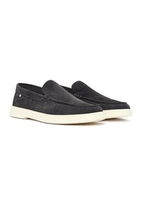Zapatos de ante negros sin cordones con una textura suave, que cuentan con una suela de goma blanca en contraste y detalles de costura sutiles en la parte superior.