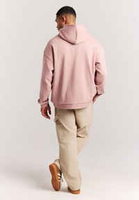 Lichtroze oversized hoodie met een capuchon, gemaakt van zachte stof. Gecombineerd met beige cargobroeken, met zijzakken en casual schoenen.