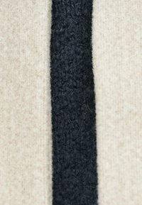 Υφασμα από μαλλί με απαλό, ανοιχτό μπεζ φόντο και υφασμένο σκούρο μπλε κάθετο ρίγες στο κέντρο. Παρουσιάζει διακριτικές διακυμάνσεις χρώματος.