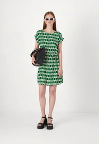 Kratka obleka zelene in bele barve z vzorcem in kratkimi rokavi, zatesnjena v pasu. Ujemajoči se s črnimi platformnimi sandalami in črno torbico.