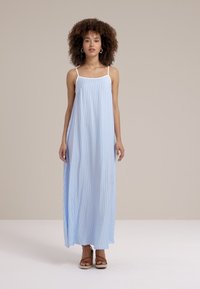 Heledad sinise triibuga maksi kleit õhukeste valgete rihmadega, mugav sobivus, voolav kanga ja sujuva tekstuuriga. Kannab beeži kandadega sandaale.