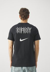 Black cotton t-shirt featuring a large white graphic "BABY" on the back and a small Nike logo. Short sleeves and round neckline.
