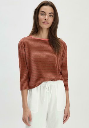 Top a righe color ruggine con scollatura a girocollo, maniche tre quarti e rifiniture rosa a contrasto; indossato con pantaloni bianchi con coulisse.
