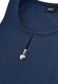 Haut sans manches bleu marine en tissu texturé, doté d'une fermeture éclair à l'avant avec un tirette en forme de cœur en argent et d'un col rond.