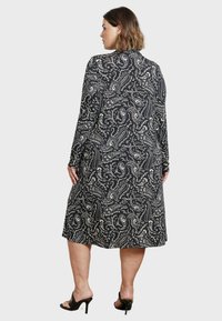 Zwart jurk met paisleypatroon, lange mouwen, knielange ontwerp, zachte stof en ronde halslijn. Zakken aan de zijkanten zijn zichtbaar.