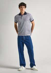 Polo tričko s krátkým rukávem s geometrickým vzorem v modré a bílé, námořnický límec, kombinované s volnými modrými džíny a bílými teniskami.