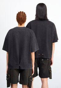 Μαύρα oversized βαμβακερά t-shirt με κοντά μανίκια, με στρογγυλή λαιμόκοψη, φορεμένα με σκούρα cargo σορτς που έχουν πλαϊνές τσέπες.
