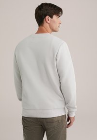 Sweatshirt texturat de culoare gri deschis, cu guler rotund și manșete ribbate. Prezentând un model subtil, este asortat cu pantaloni de culoare verde măsliniu.