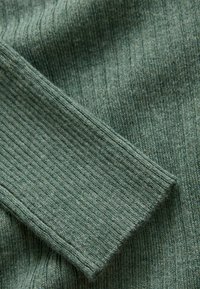Grüner gerippter Stoff mit einer weichen Textur, der eine nahtlose Manschette aufweist. Das Material sieht gestrickt und leicht flauschig aus.