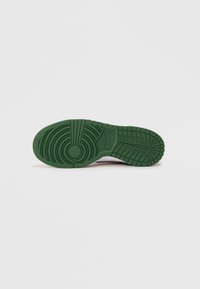 Sola de borracha verde com padrão de piso texturizado, apresentando designs circulares e em grelha para tração, na parte inferior de um ténis em rosa e branco.