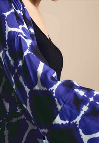 Blauw-wit gestreepte kimono met een losse pasvorm, gemaakt van lichte stof. Bevat brede mouwen en een diep V-hals zwart top eronder.