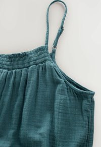 Teal ärmlös topp gjord av strukturerad väv, med en smockad bål och justerbara axelremmar med metallbeslag.