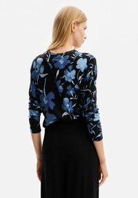 Maglione nero con motivi floreali blu, scollatura rotonda e maniche lunghe. Il retro presenta un elemento di design distintivo con una finitura a contrasto.