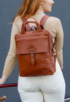 Brown leather backpack with a top handle, adjustable straps, front flap with buckle, and side zipper pocket. Smooth texture with minimal hardware.