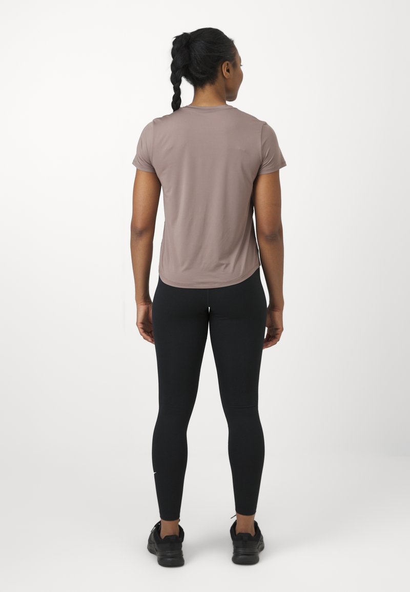 Maglietta sportiva a maniche corte color malva abbinata a leggings neri. Tessuto morbido, design aderente e orlo arrotondato. Scarpe sportive nere.